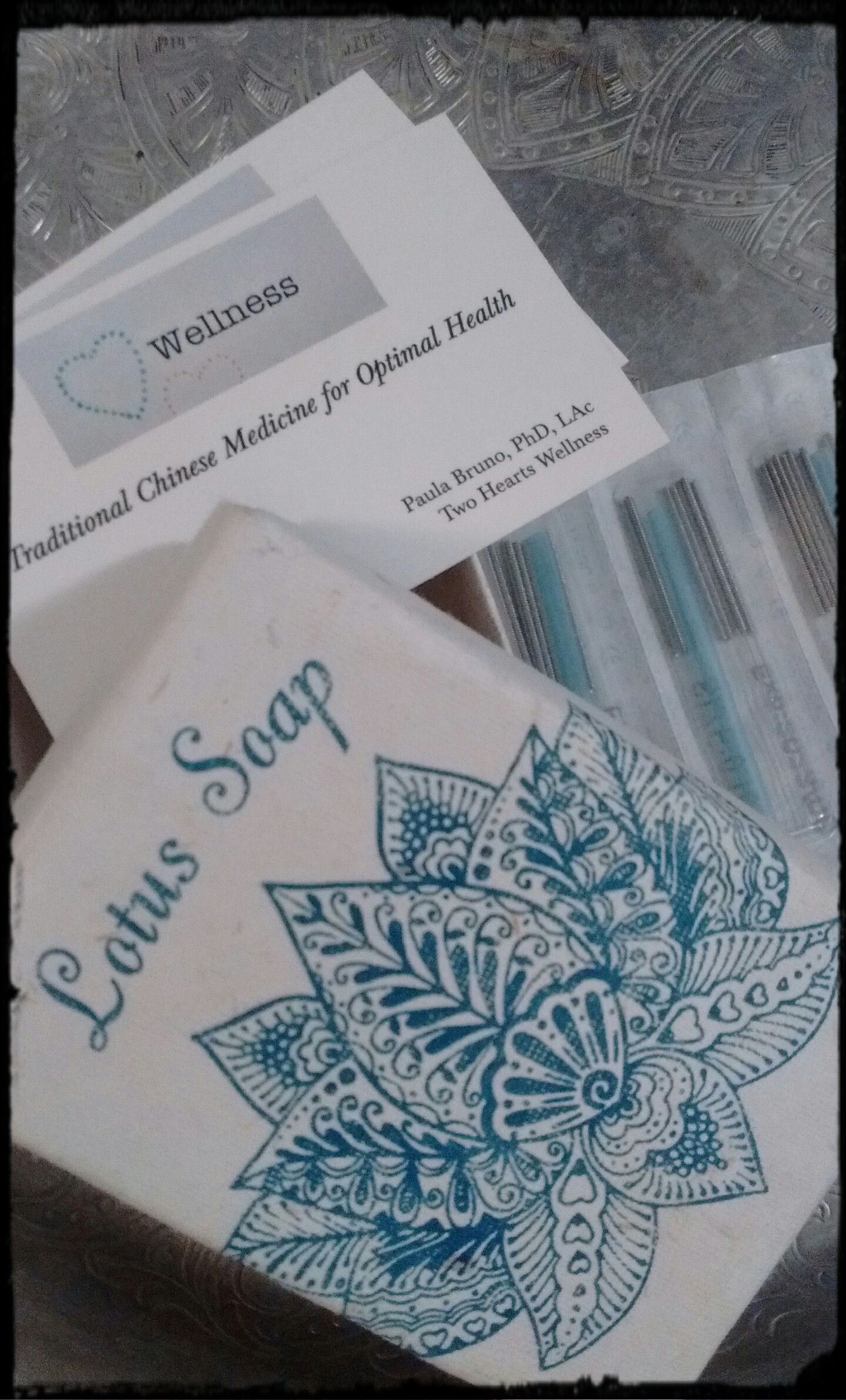 Two Hearts Wellness business card, acupuncture needles in 10-pack packets, & lotus soap package